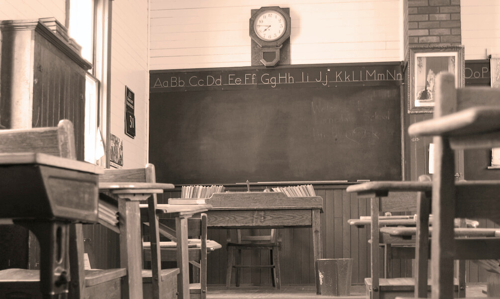 Vintage early 1900's classroom in sepia showing desks and the teacher's desk from down the aisle