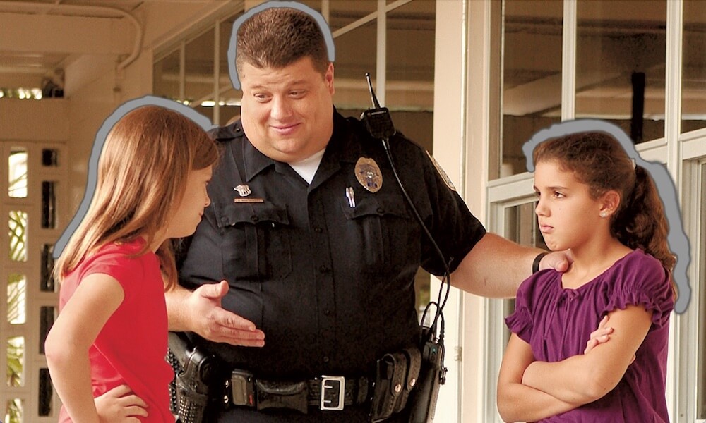 Police officer standing between two girls looking at each other angrily