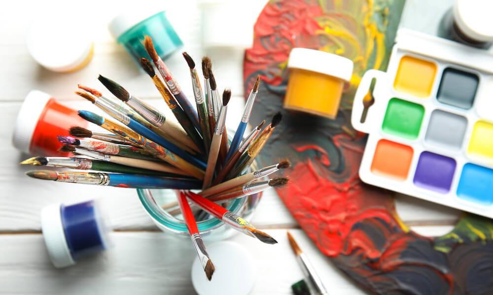 Glass jar with brushes, paints and palette on wooden background, top view