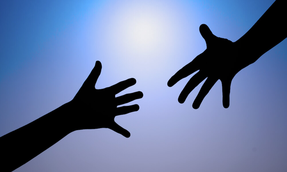 Hands reaching for each other against blue sky