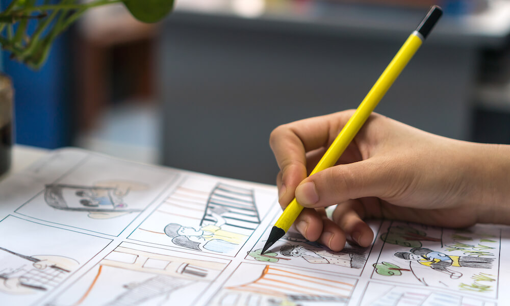 Close up of illustrator's hand drawing a graphic novel with a colored pencil