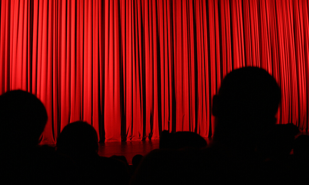 An audience facing the stage during an intermission with the curtains drawn.