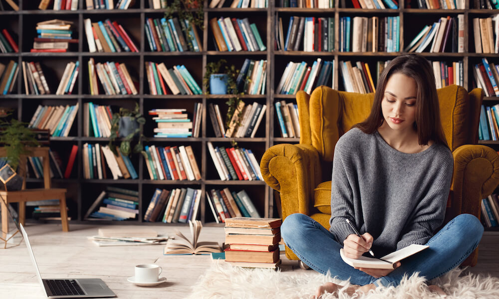 Young woman writer in library at home creative occupation sitting writing notes