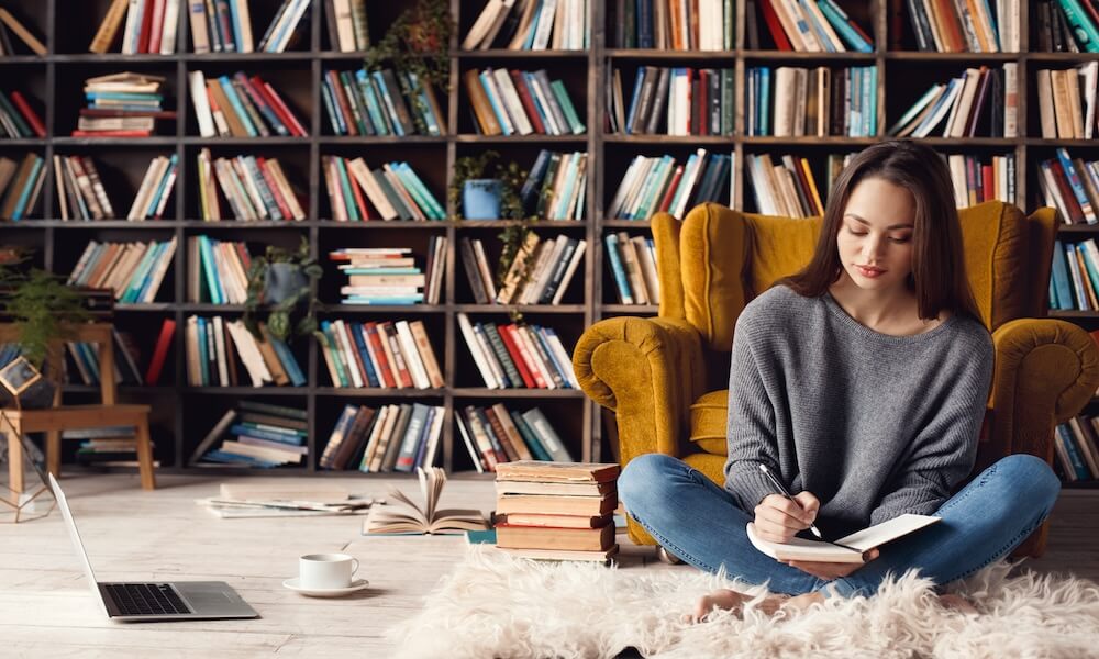 Young woman writer in library at home creative occupation sitting writing notes