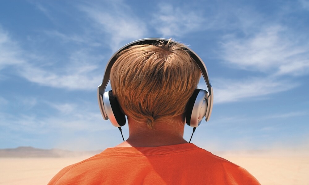 Back view of young boy standing outdoors with headphones