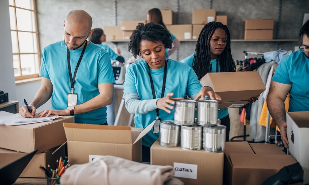 Multi-ethnic group of people, diverse volunteers packing donation boxes in charity food bank.