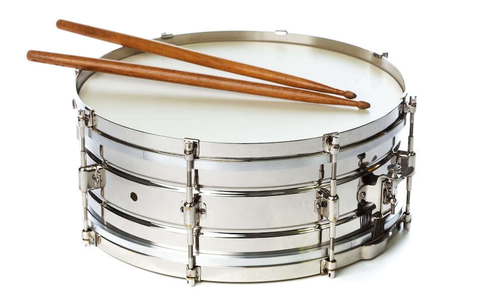 A silver chrome snare drum with drum sticks isolated on a white background.