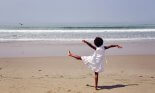Rear view of an african american girl standing on one leg on the beach