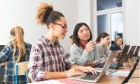 Group of female students coding on laptops in a computer lab. Close up of asian and afro american young women discussing.