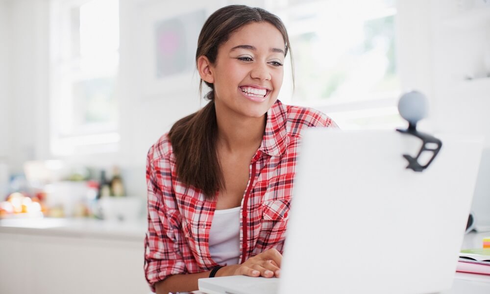 Smiling teenage girl enjoying video chat on laptop.