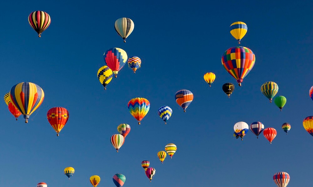 Many vividly colored hot air balloons float in the sky.