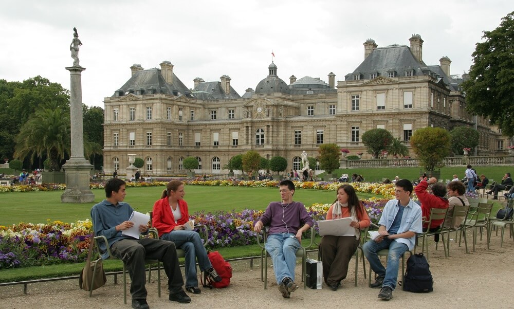 Friends enjoying a day outside at Jardin Du Luxembourg listening to music on MP3 player, reading books, sketching in a sketchpad. drawing, shopping bags, studying, Palais du Luxembourg in the background. (models: Rachida Ammour, teen girl, Asian, Arabic French caucasian; Agathe DeDrouas, teen girl, French caucasian; Tristan Fevre and Aymeric Fevre, twin teen boys, French caucasian; Skan Guenin, teen boy, multiethnic French), Paris, France