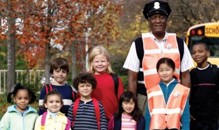 A friendly school-bus driver standing with a group of smiling kids on their way to school.