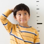 Asian boy standing next to height markers on wall