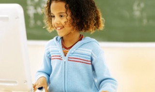 A smiling girl works at a computer in a classroom. A smiling girl works at a computer in a classroom.