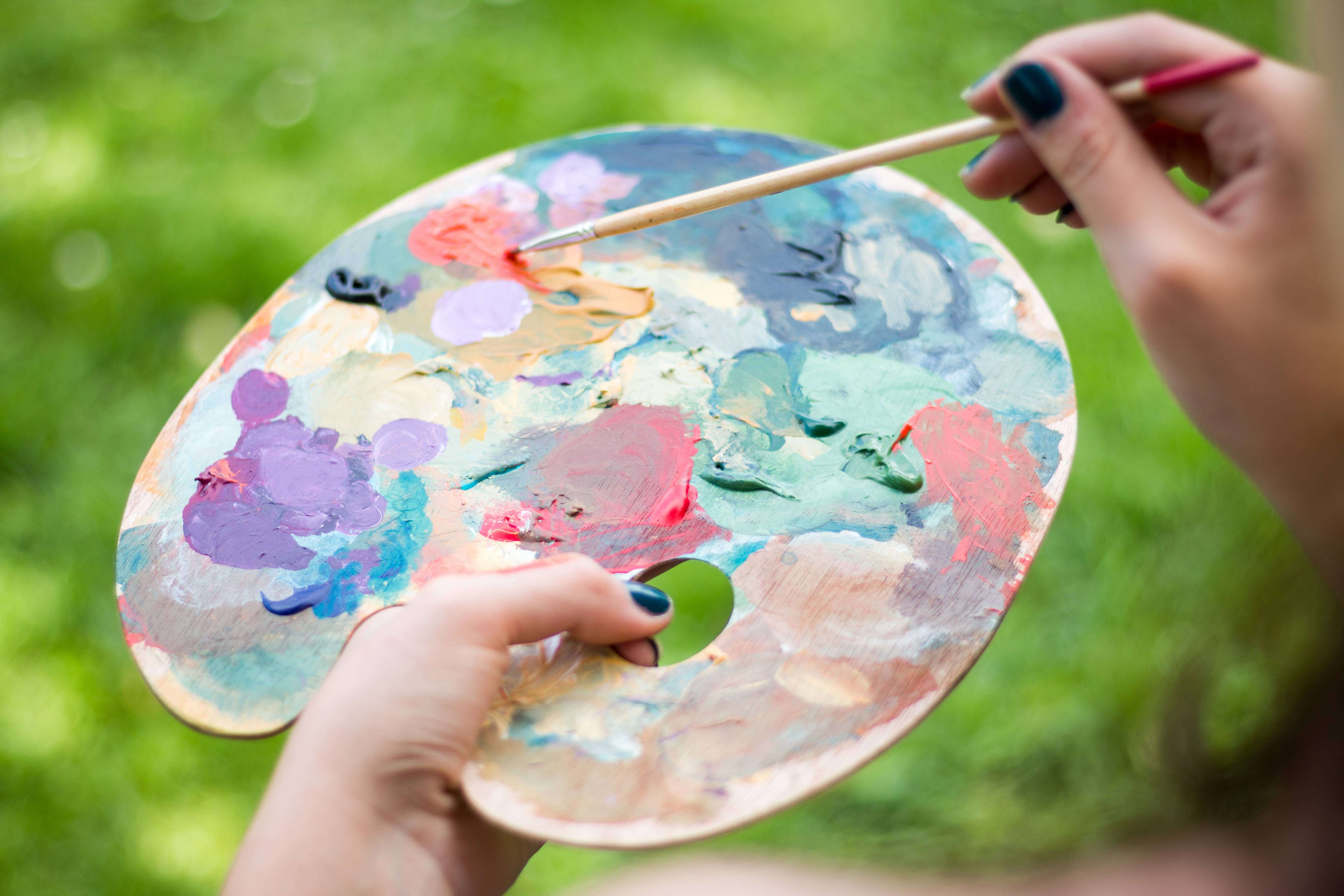 Woman artist painting outside and holding a palette of colorful paints in her hand.