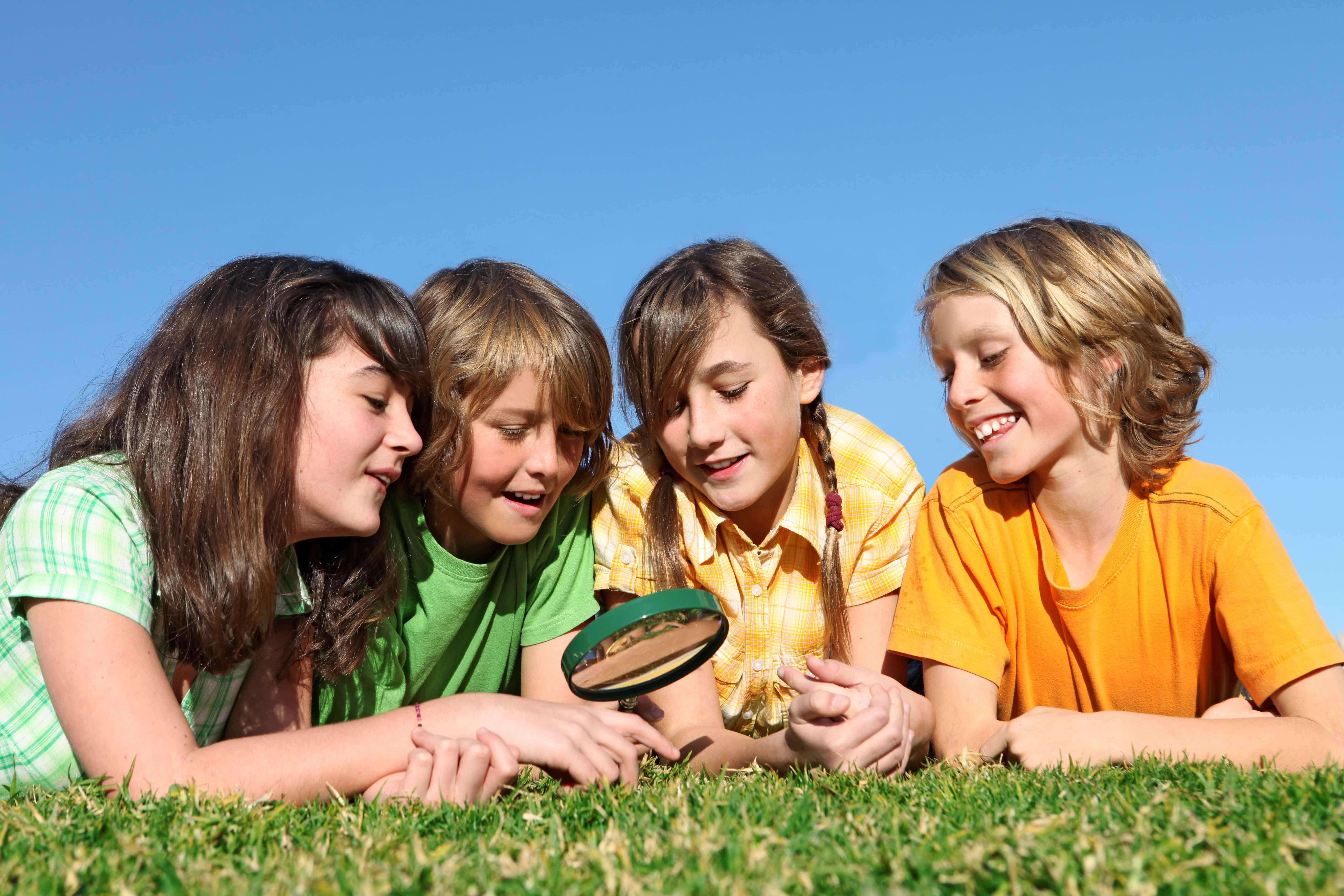 Four kids look at the grass through a magnifying glass.