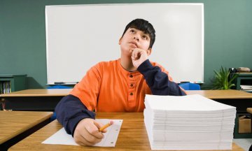 Schoolboy thinking, with a stack of notepaper on his desk