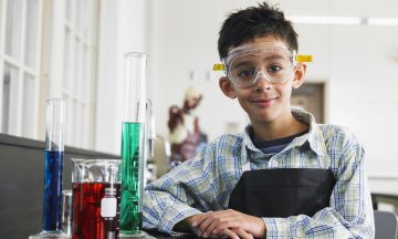 Boy standing beside assorted beakers in school laboratory