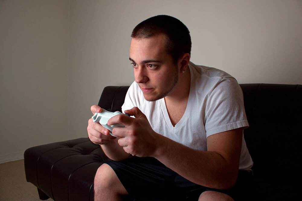 Young man playing a video game in a room lit by the television monitor