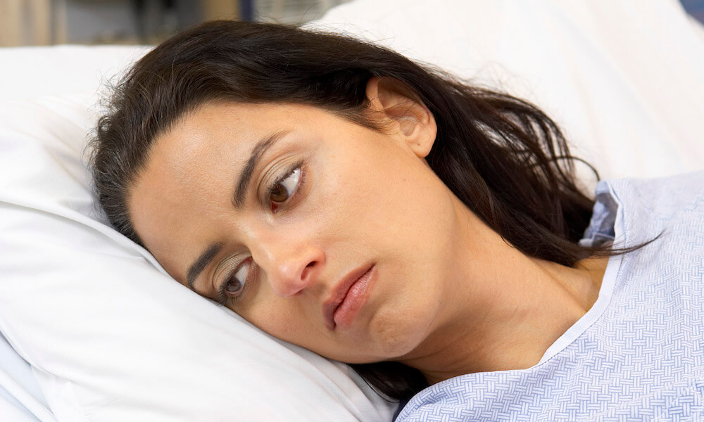 Una mujer que se ve enferma descansa en una cama de hospital