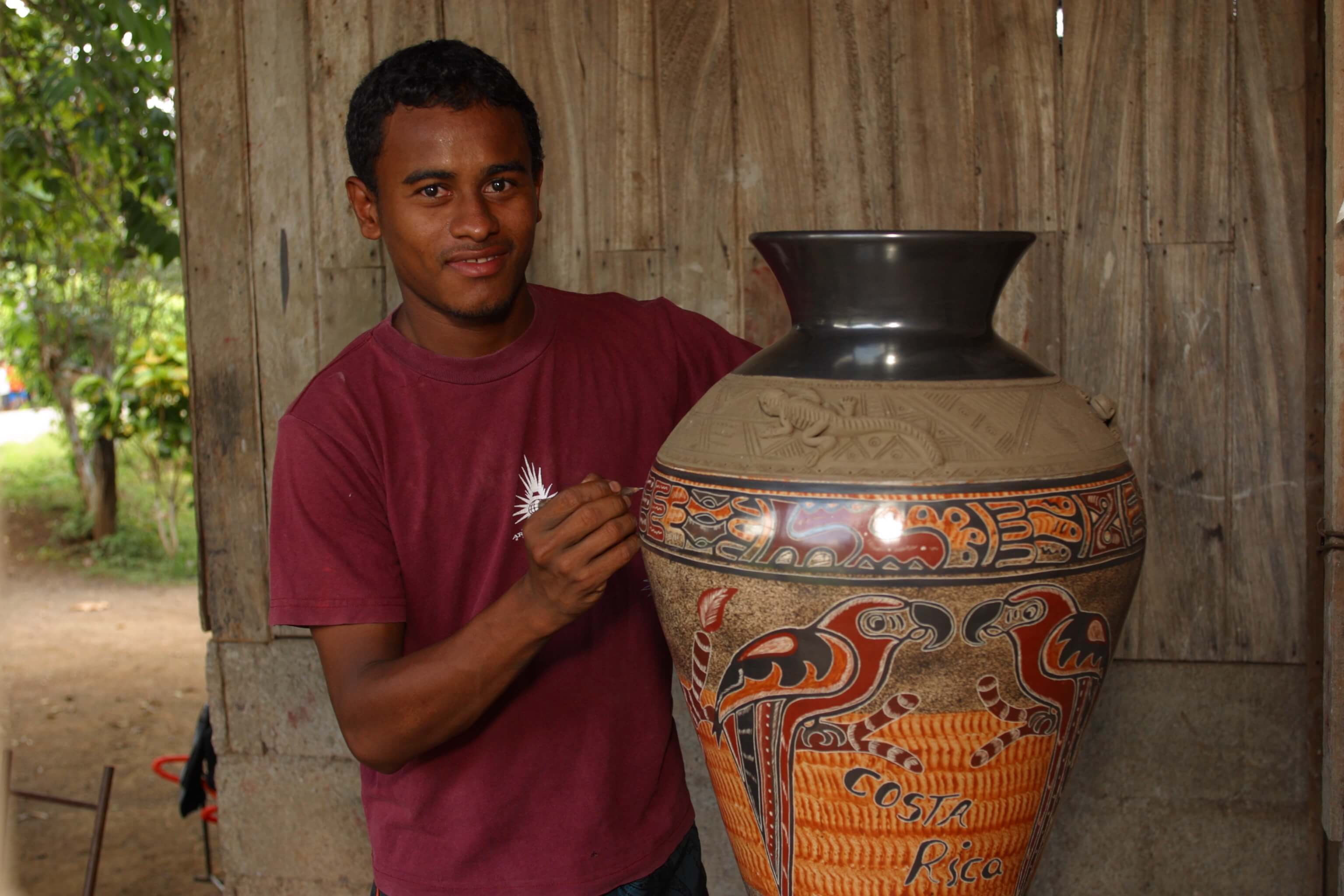 An artist from the Chorotega indigenous group in Costa Rica paints a colorful design on a large clay vase.