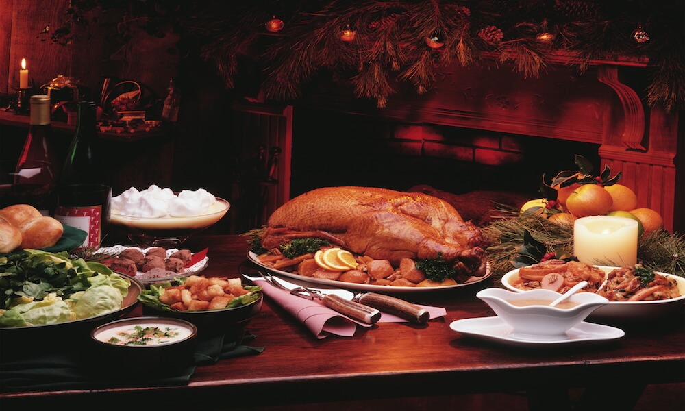 Una mesa puesta con una comida de Navidad. Hay pavo asado, verduras y postre.