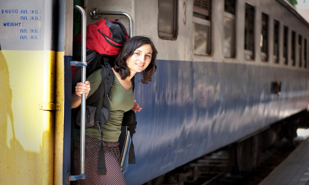 A female traveler carrying a backpack is disembarking from a train.