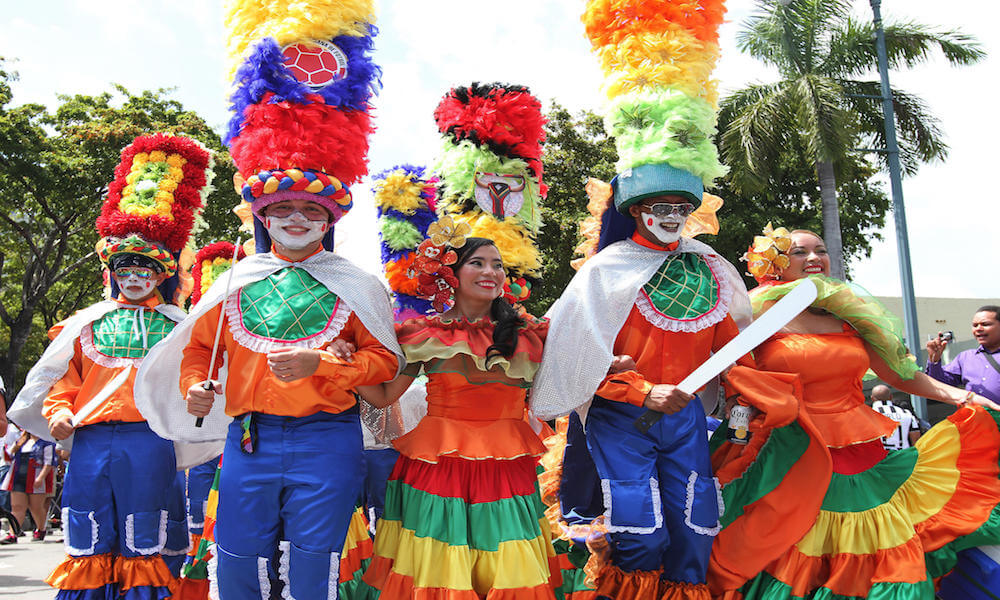 A group of Colombians in colorful, traditional clothing marches in a parade.