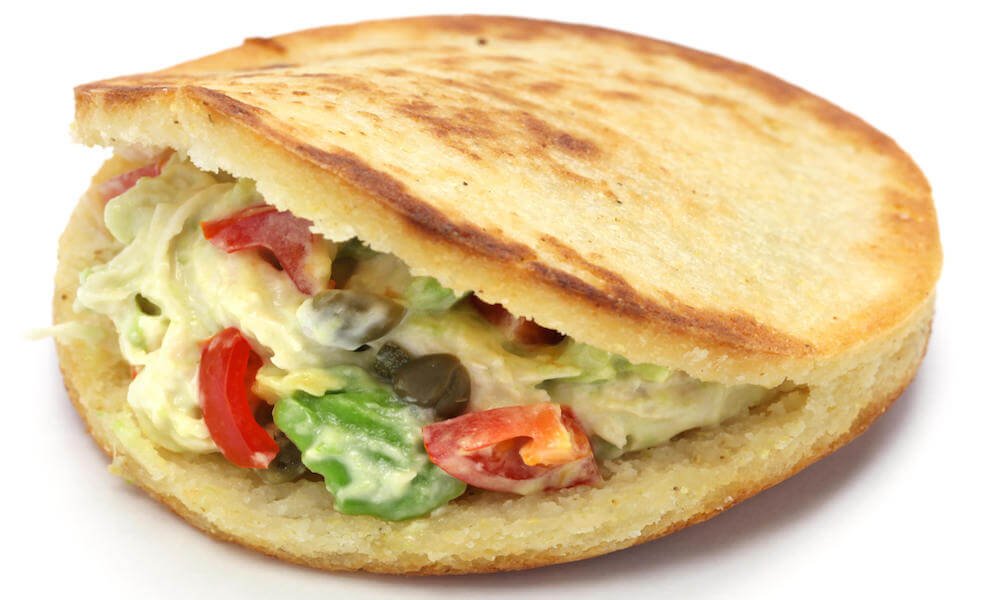 An arepa, a sandwich made of ground corn meal, stuffed with a filling of cheese, lettuce, and tomato.