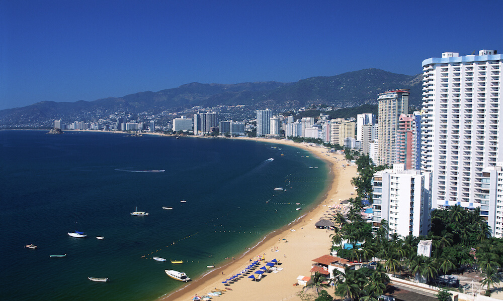 Los hoteles rodean las playas de Acapulco. Lanchas y barcos de vela están en la bahía.