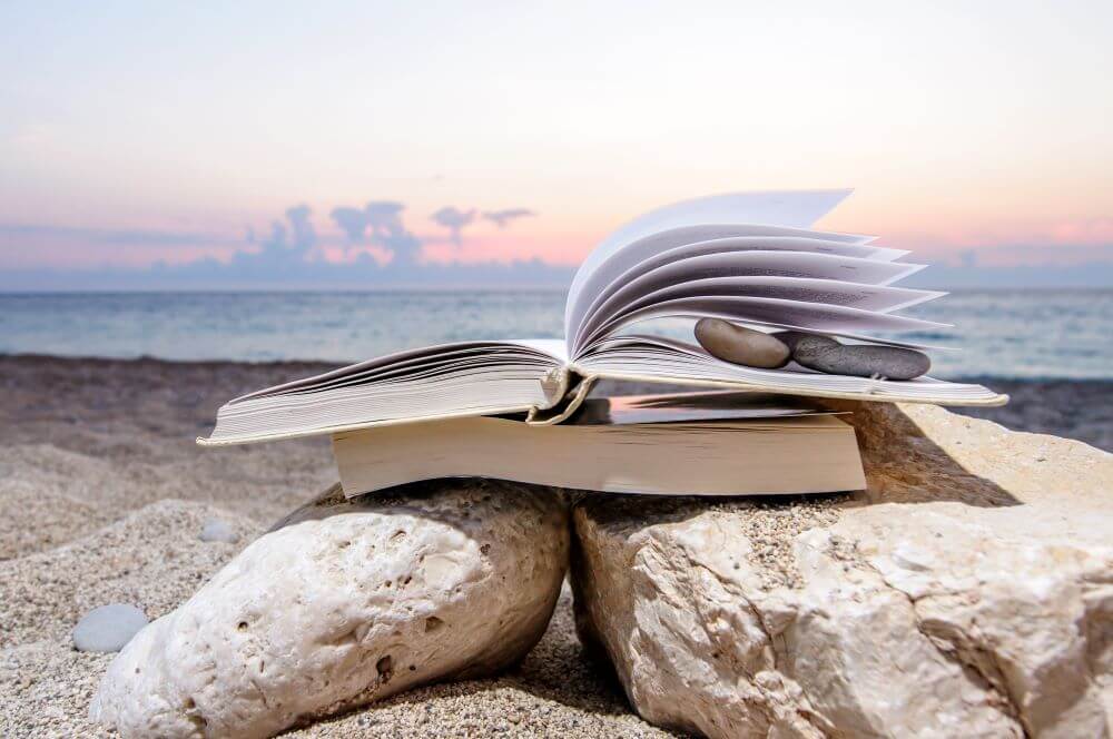 Open book at beach near the sea during sunset placed over other books on rocks
