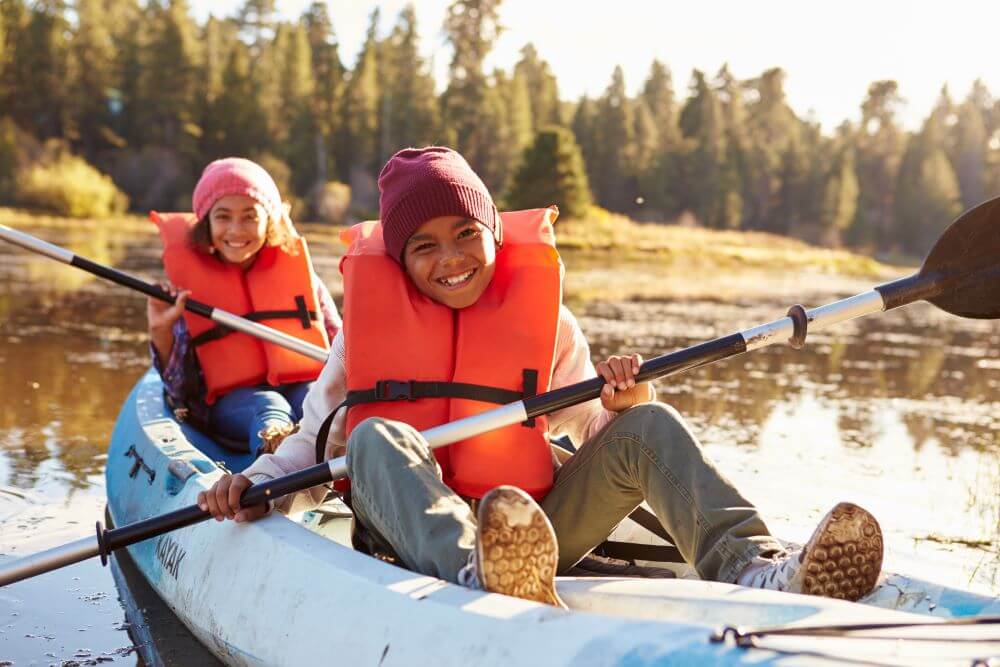 Two Children Rowing Kayak On Lake