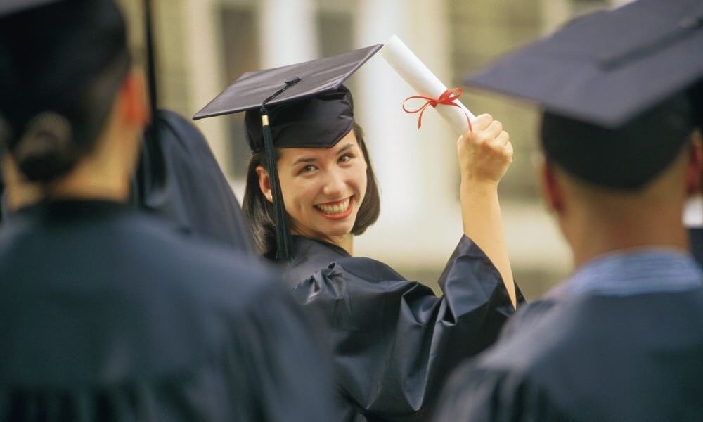 Woman at graduation holding diploma, looking over her shoulder